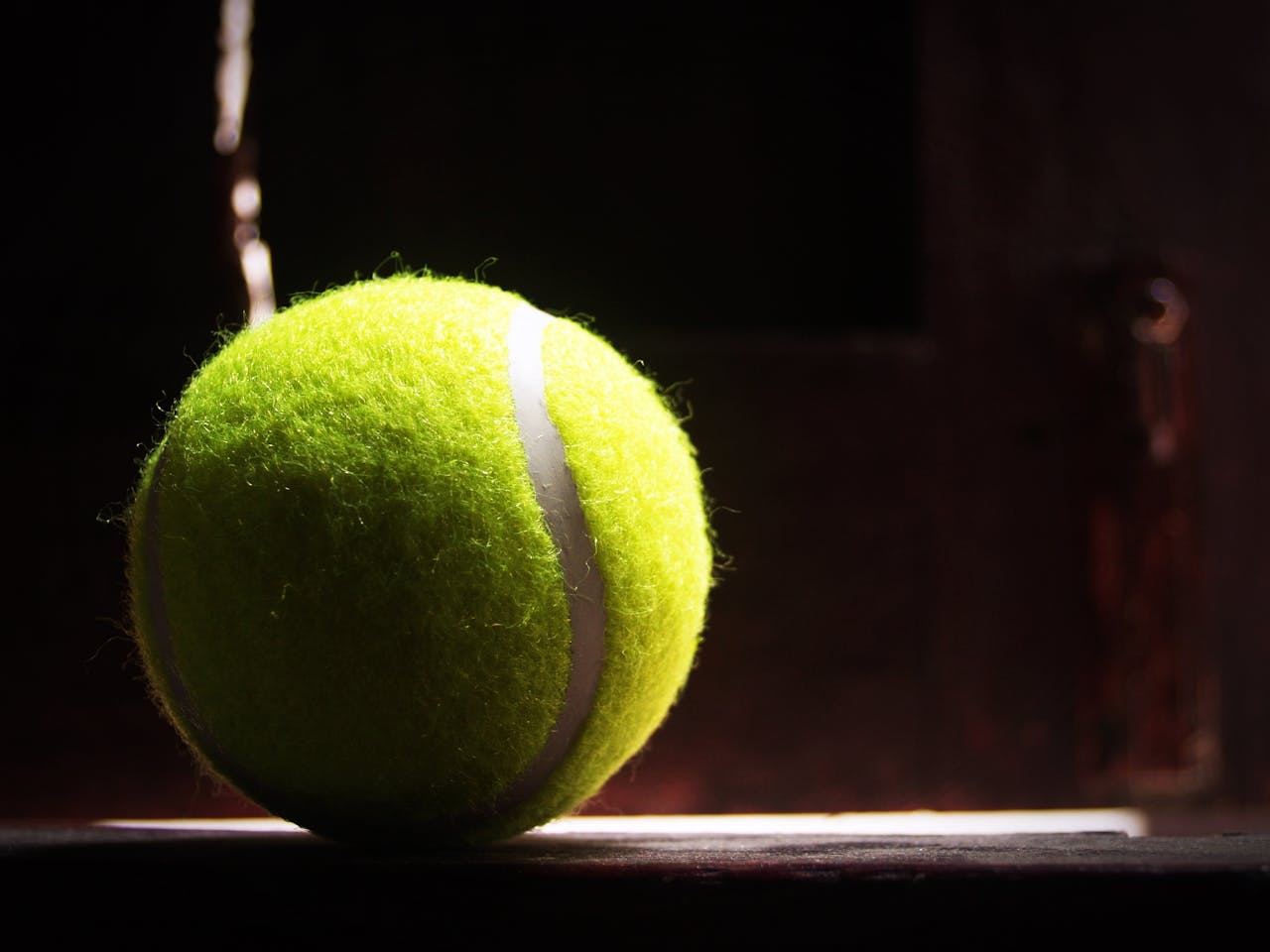 A tennis ball illuminated by dramatic lighting, highlighting its texture and vibrant color.