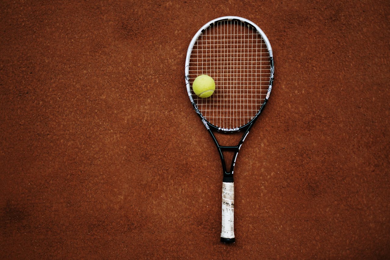 Tennis racket and ball on clay court, perfect for sports imagery.
